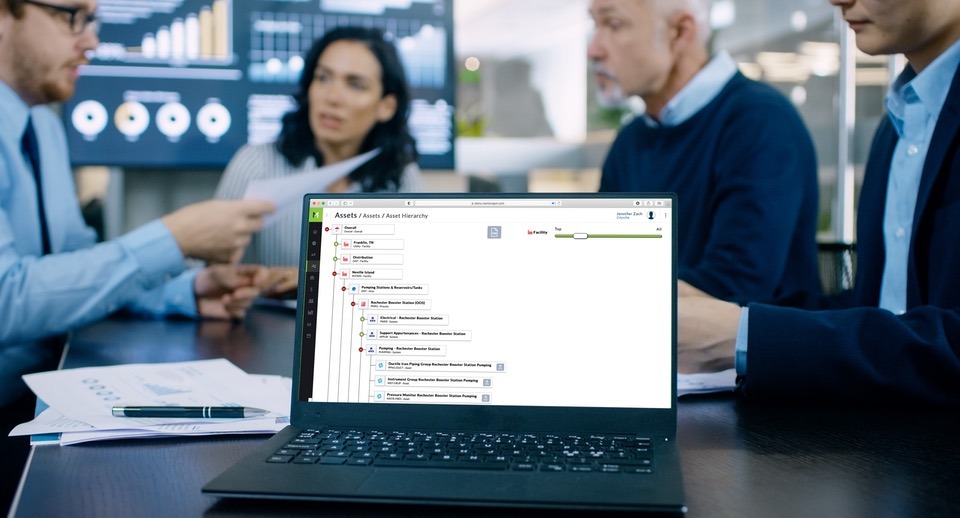 MentorAPM asset hierarchy dashboard being reviewed on a laptop in a client meeting